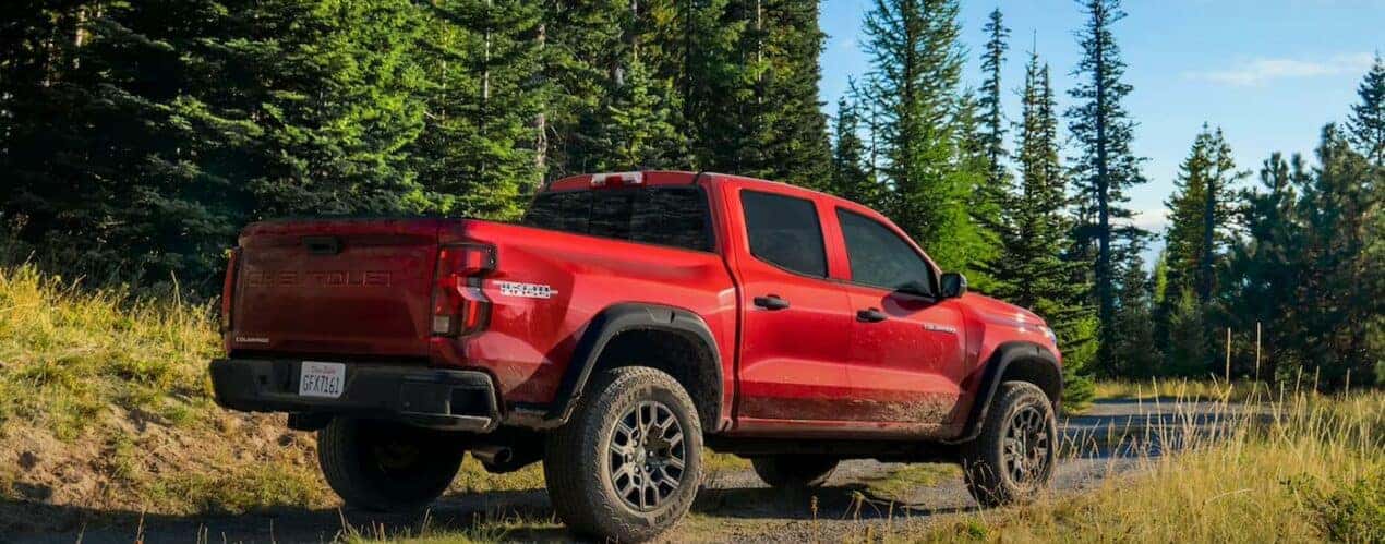 A red 2023 Chevy Colorado Trail Boss is shown from a rear angle on a muddy dirt road.