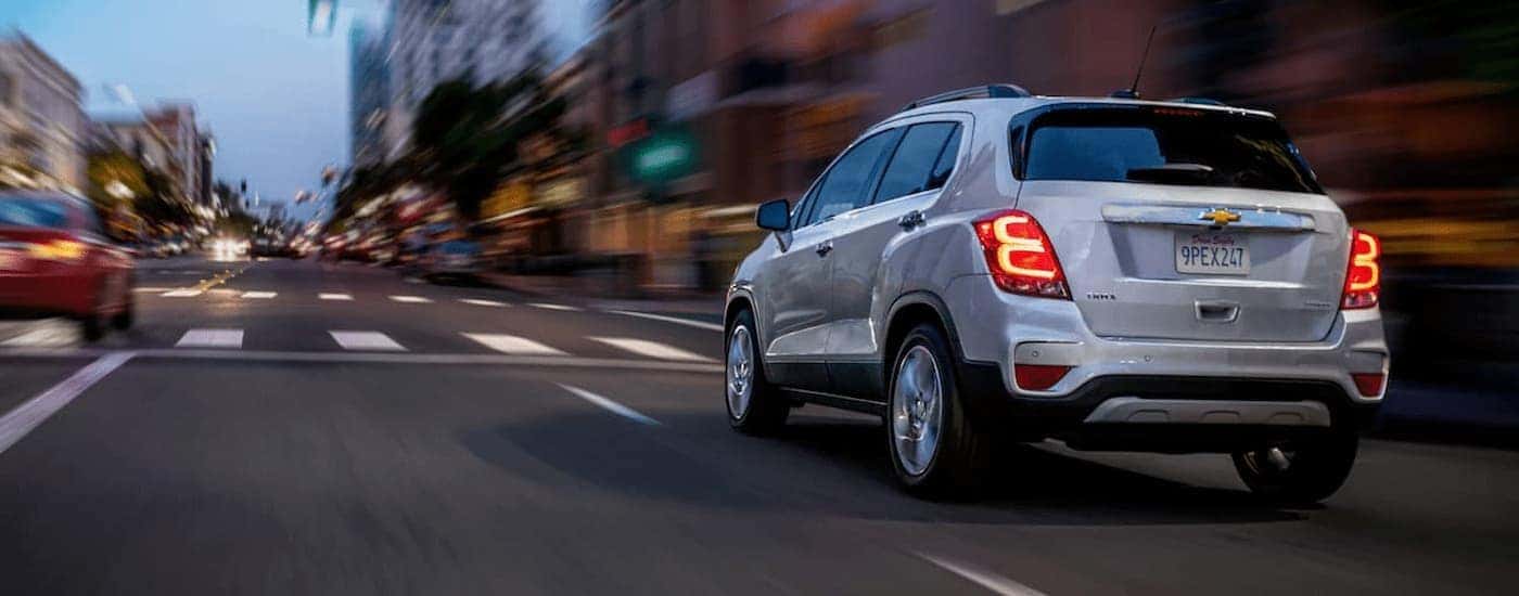 A silver 2020 Chevy Trax is shown from the rear driving on city street.