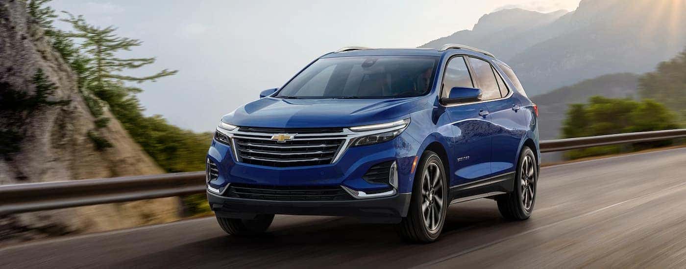 A blue 2023 Chevy Equinox is shown driving on a mountain highway.
