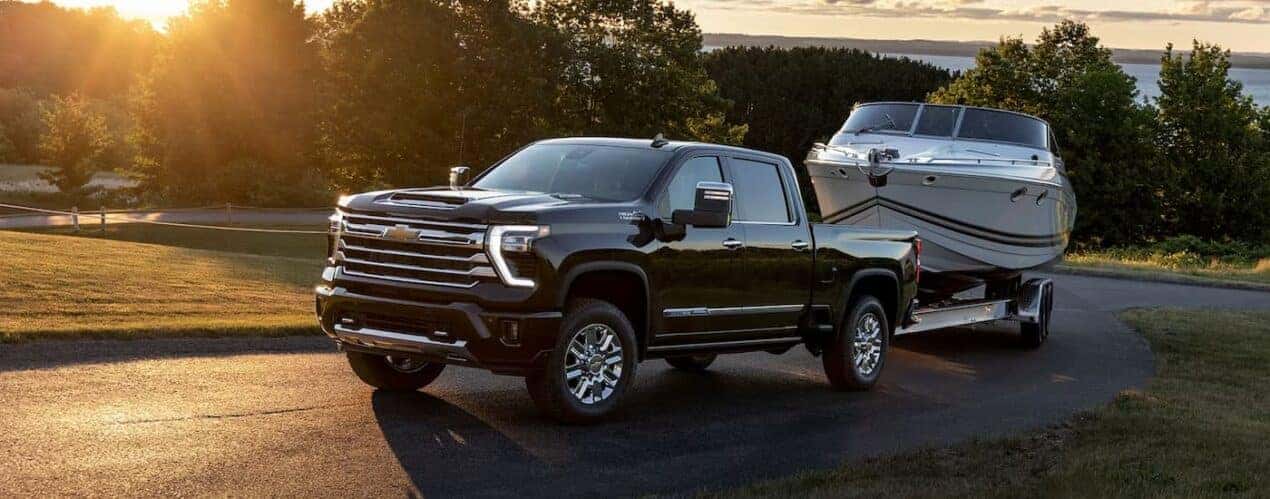 A black 2024 Chevy Silverado 2500 HD is shown towing a white boat on a winding road.