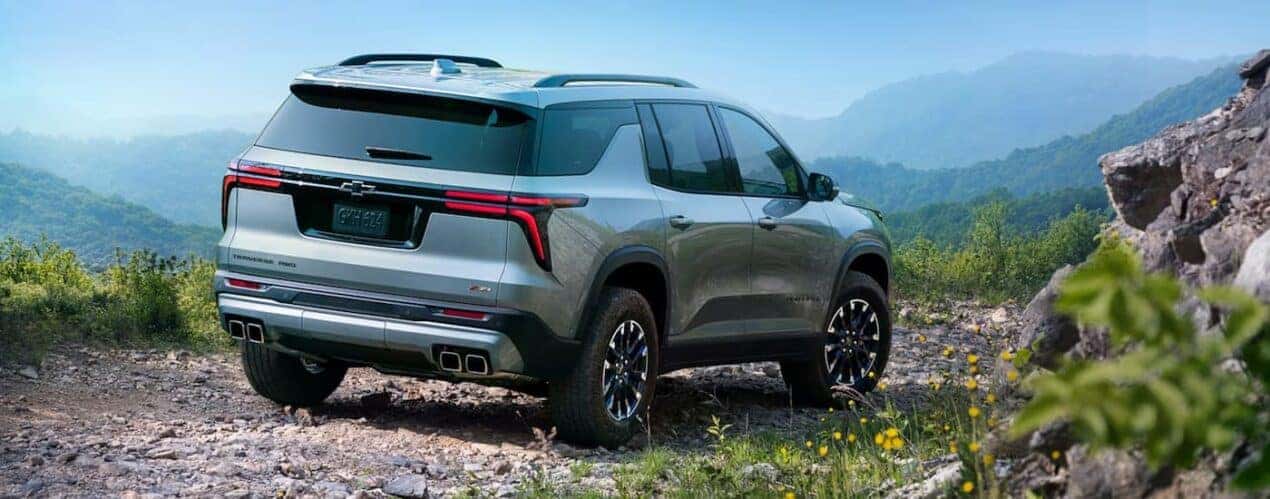 A grey 2023 Chevy Traverse Z71 is shown from a rear angled driving down a gravel mountain road.
