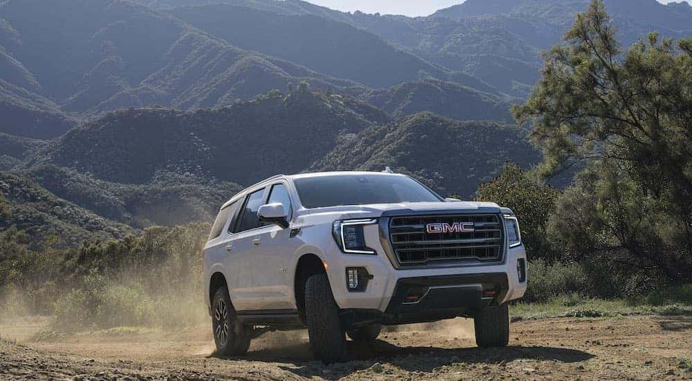 A white 2022 GMC Yukon AT4 is shown from the front at an angle after leaving a dealer that has used SUVs for sale.