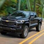 One of many popular Chevy trucks for sale, a black 2023 Chevy Colorad, is shown driving on a bridge.