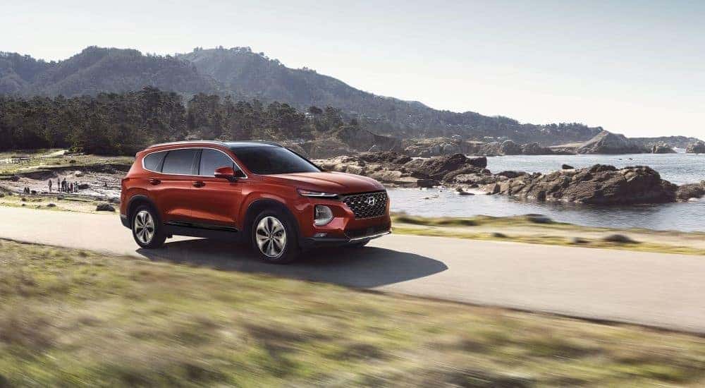 A red 2019 Hyundai Santa Fe is shown driving near an ocean.