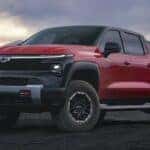 One of many popular Electric vehicles for sale, a red 2024 Chevy Silverado EV Trail Boss, is shown parked off-road.