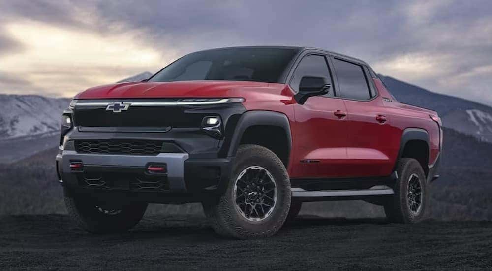 One of many popular Electric vehicles for sale, a red 2024 Chevy Silverado EV Trail Boss, is shown parked off-road.