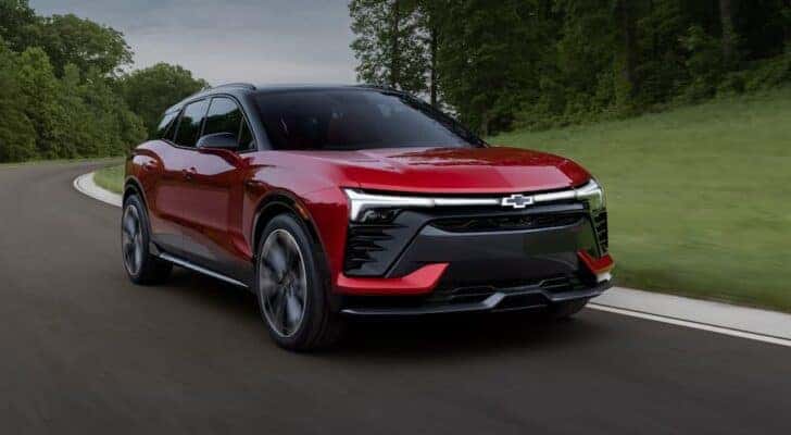 A red 2024 Chevy Blazer EV SS is shown driving on a winding road after viewing electric vehicles for sale.