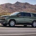 A sage green 2024 Chevy Suburban LT driving on an open road.