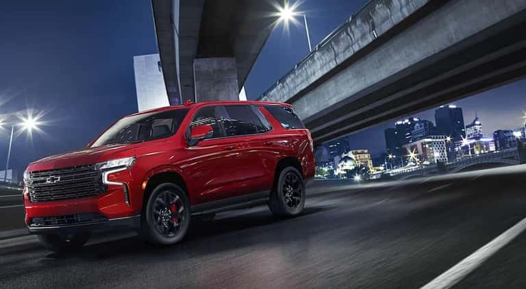 A red 2024 Chevy Tahoe RST driving under a bridge at night.