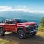 A red 2024 Chevy Colorado driving on a mountain path with bikes in the back.