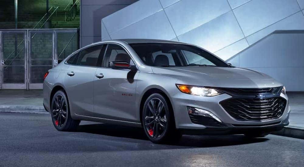 A silver 2024 Chevy Malibu 1LT is shown parked near glass doors.