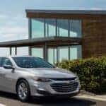 A popular Chevy Malibu for sale, a silver 2024 Chevy Malibu, is shown parked near a house.