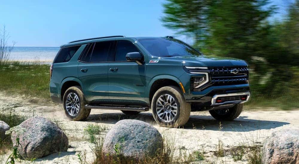 A green 2025 Chevy Tahoe driving on the beach past large rocks.