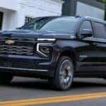 A blue 2025 Chevy Suburban for sale is shown driving on a street.