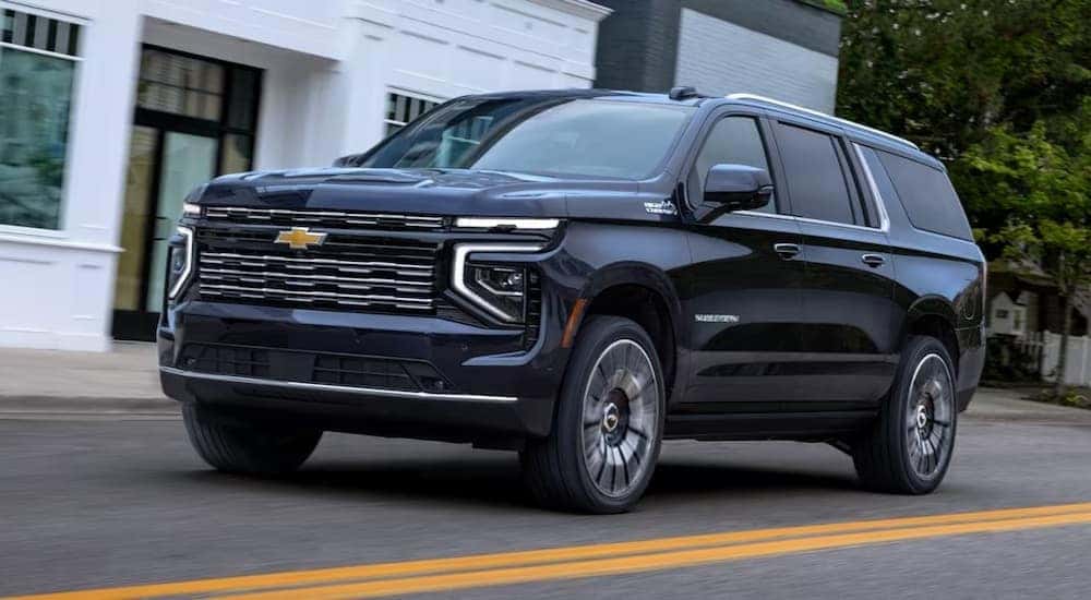 A blue 2025 Chevy Suburban for sale is shown driving on a street.