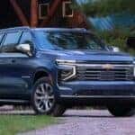 A blue 2025 Chevy Suburban is shown parked near a log cabin.