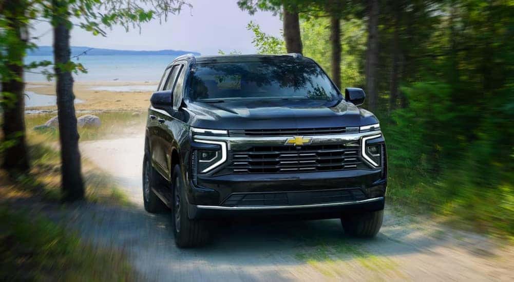 A blue 2025 Chevy Suburban is shown driving on a sandy path.