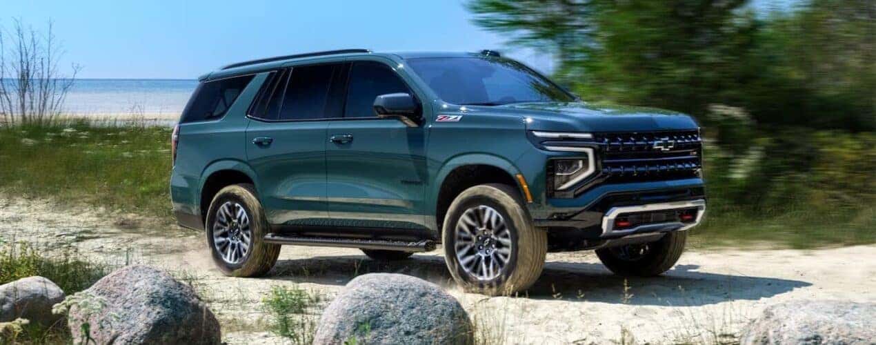 A green 2025 Chevy Suburban is shown parked off-road on a shore.