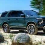 A green 2025 Chevy Tahoe Z71 is shown driving near an ocean.