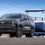 A black 2025 Chevy Suburban High Country is shown from the front at an angle while towing a boat.