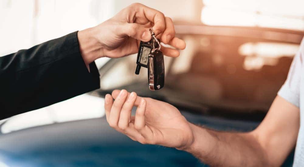 A salesman is handing keys to a customer after they bought a car.