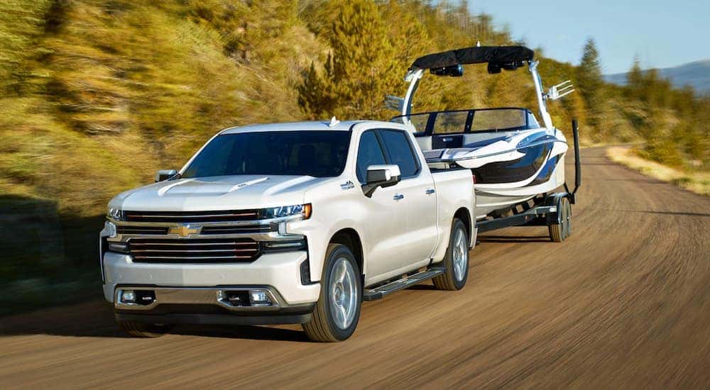 A white 2021 Chevy Silverado 1500 High Country towing a boat.