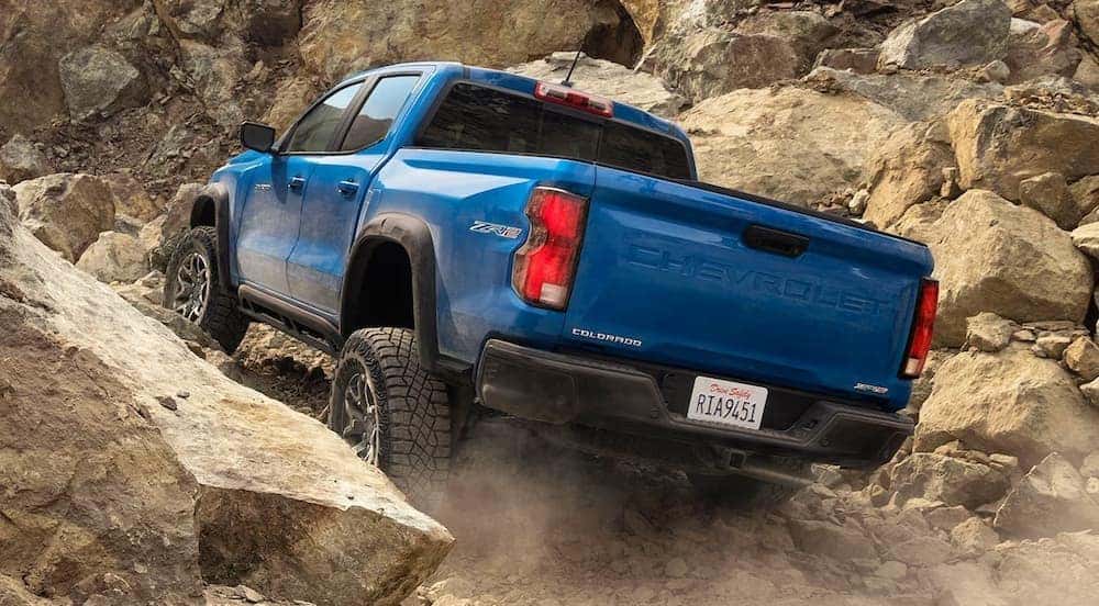 A blue 2024 Chevy Colorado ZR2 is shown driving off-road on boulders.