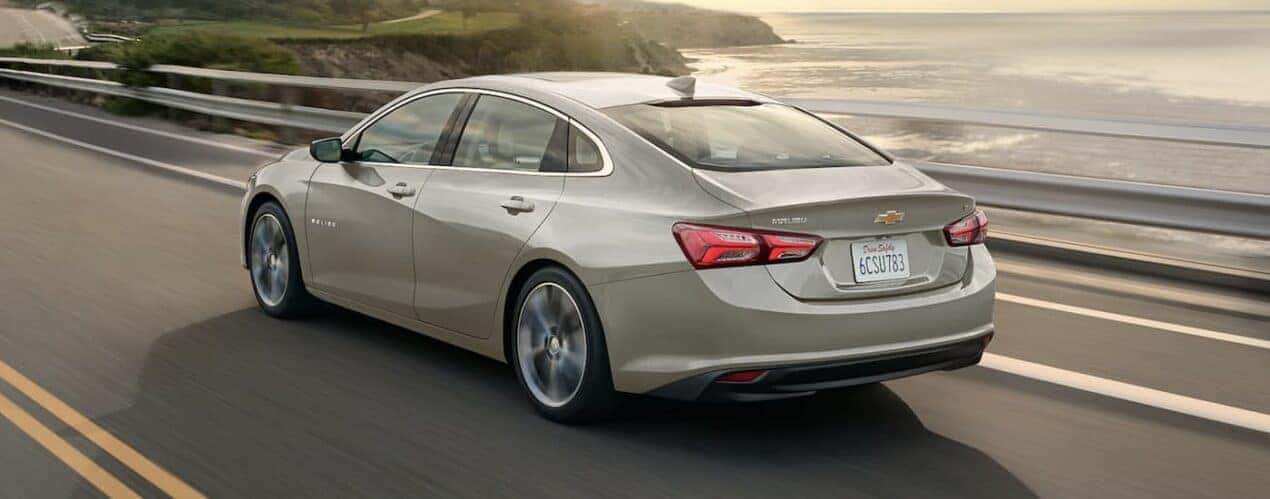 A rear view of a beige 2024 Chevy Malibu driving.