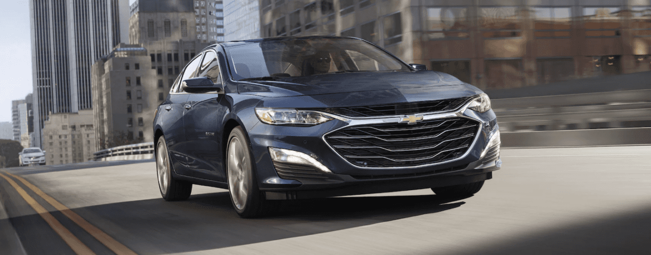 A blue 2024 Chevy Malibu driving in a city.