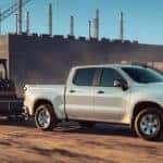 A white 2024 Chevy Silverado 1500 Custom is shown towing a trailer.