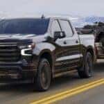 A black 2024 Chevy Silverado 1500 High Country is shown towing a trailer on a highway.