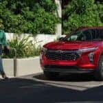 Two people walking by a red 2024 Chevy Trax RS parked by a curb.