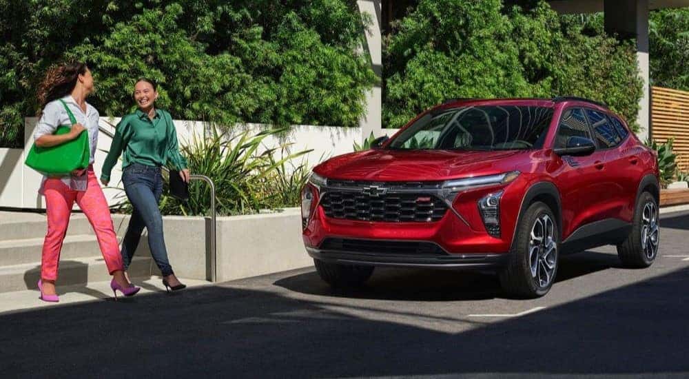 Two people walking by a red 2024 Chevy Trax RS parked by a curb.