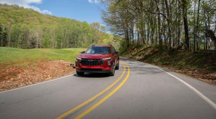 A red 2024 Chevy Trax RS driving on a rural road.