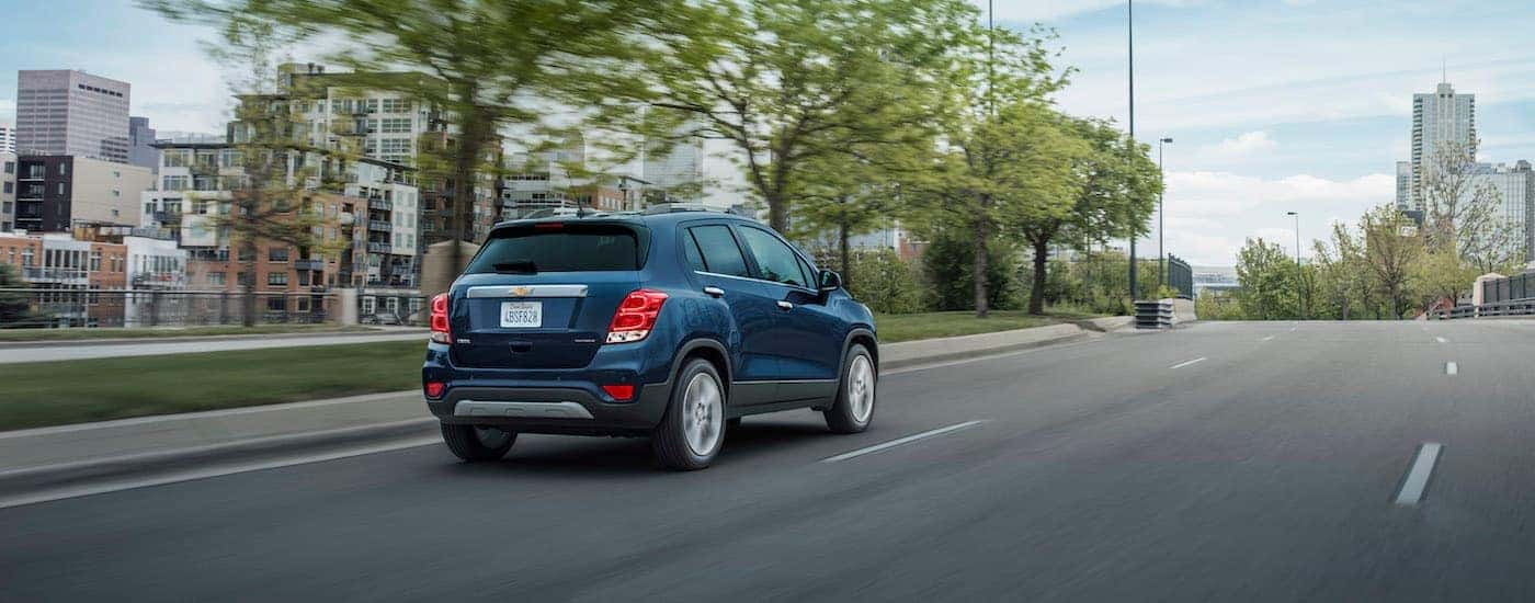 Rear view of a blue 2020 Chevy Trax driving on a tree-lined boulevard.