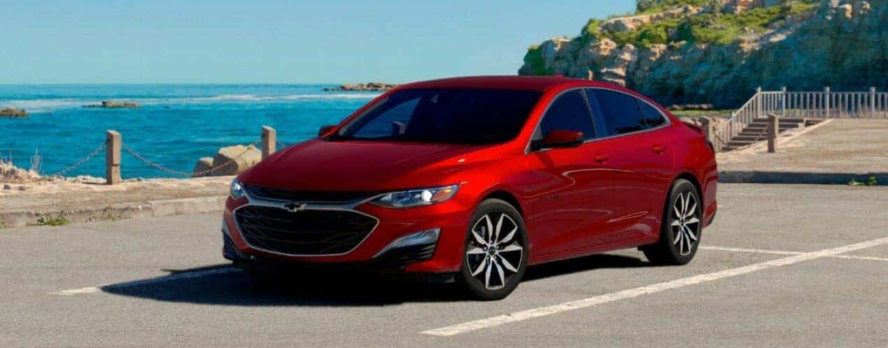 A red 2024 Chevy Malibu is shown parked near an ocean.
