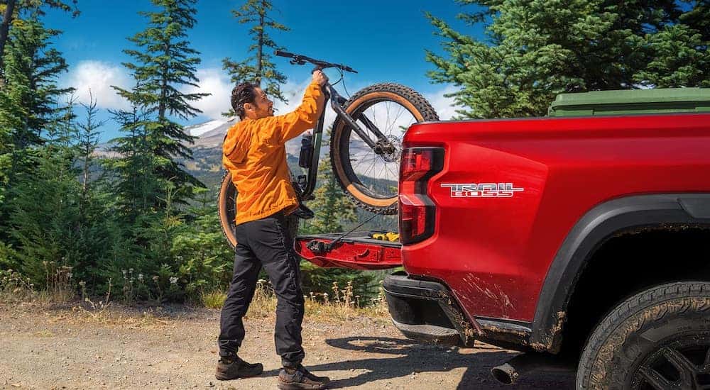 A man is shown loading a bike into the back of a 2023 Chevy Colorado Trail Boss.