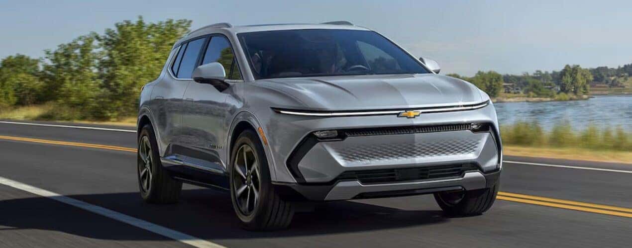 A silver 2024 Chevy Equinox EV is shown driving near a pond.