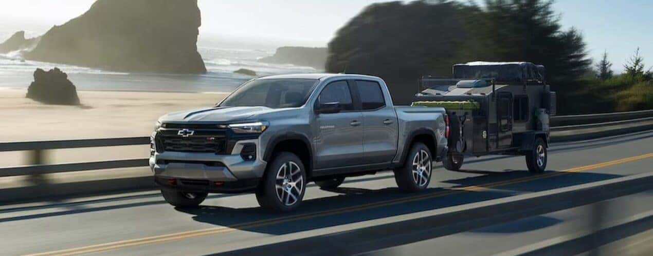 A silver 2024 Chevy Colorado Z71 is shown towing a trailer on a highway.