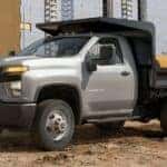 A popular used Chevy Silverado for sale in Albany, a silver 2021 Chevy Silverado 3500 Chassis, is shown parked on a construction site.