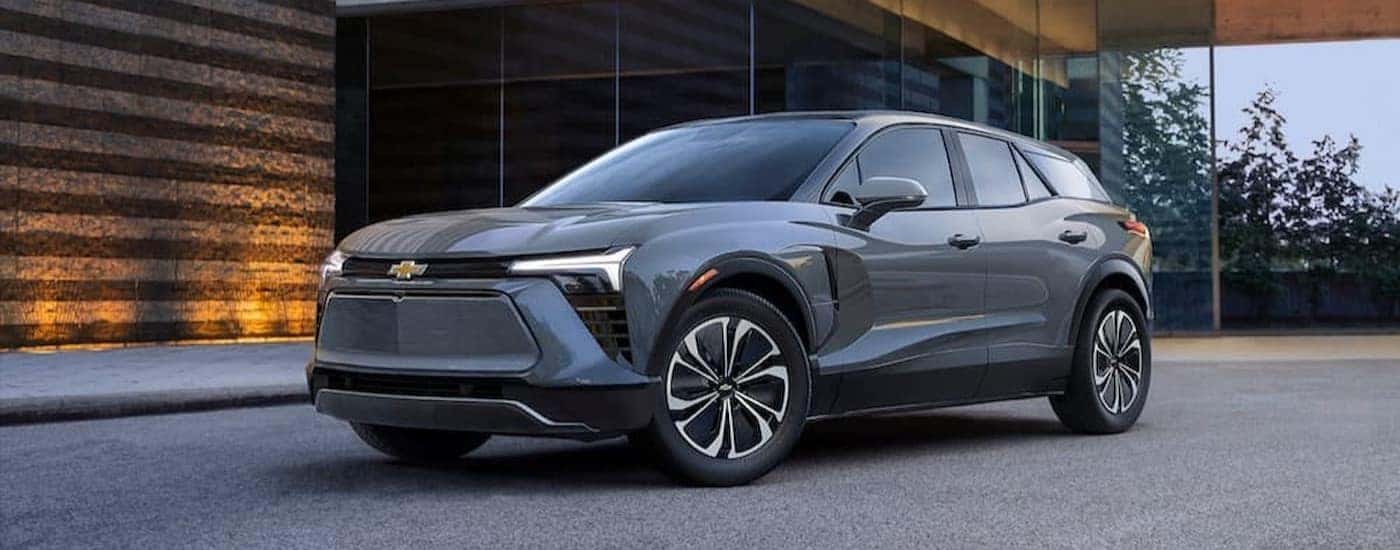 A gray 2024 Chevy Blazer EV is shown parked near a lit wooden wall and windows.