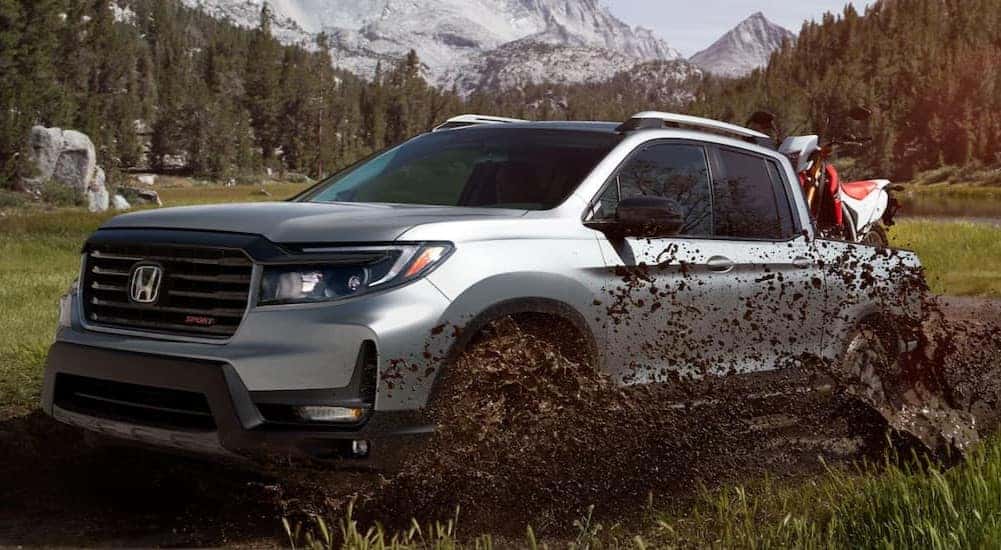 A silver 2024 Honda Ridgeline Sport is shown driving through mud.
