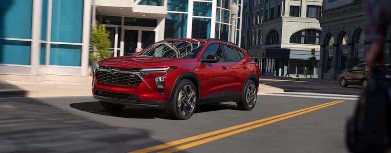A red 2025 Chevy Trax RS is shown driving on a city street.
