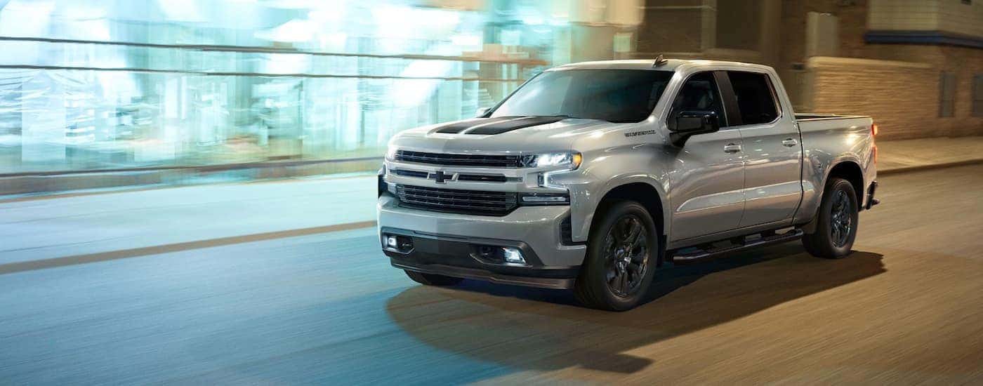 A silver 2023 Chevy Silverado 1500 RST Rally is shown driving on a city street.
