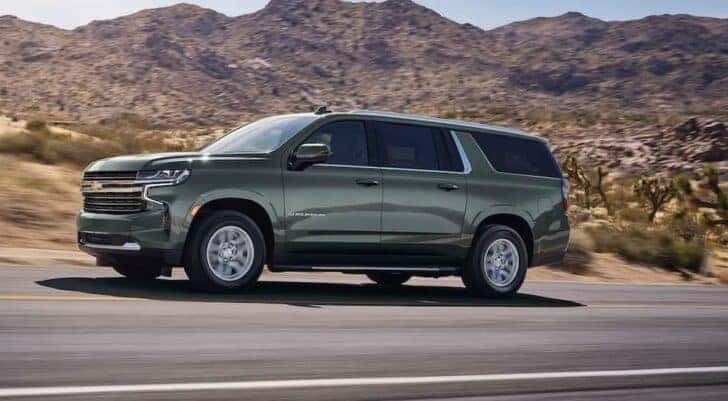 A popular used Chevy for sale near Colonie, a green 2023 Chevy Suburban, is shown driving on a highway.