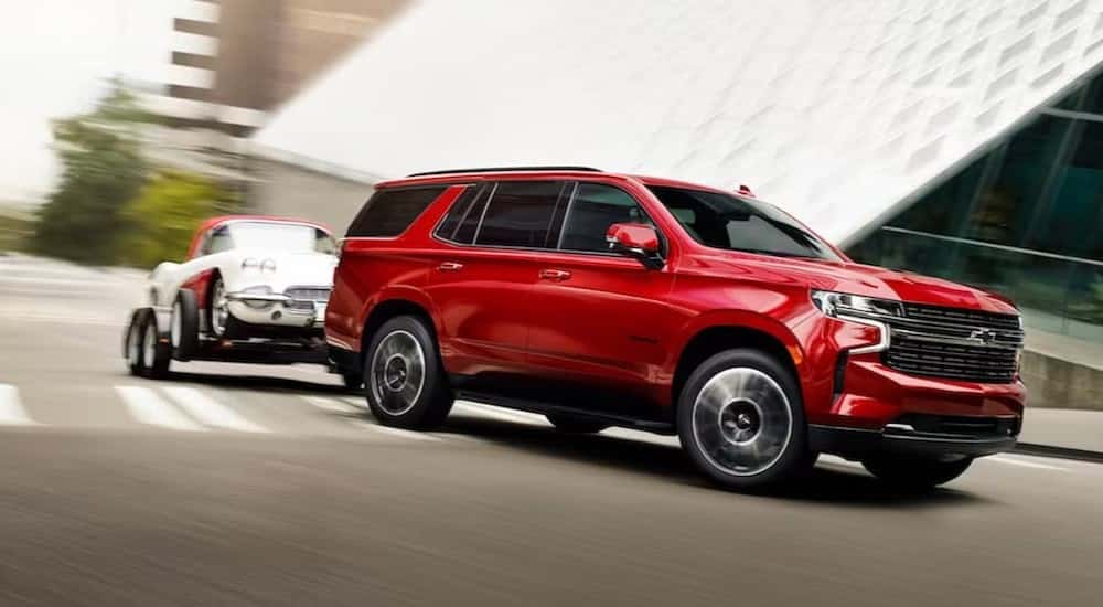 A red 2024 Chevy Tahoe is shown towing a trailer on a city street.