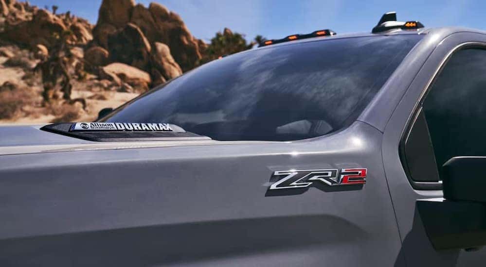 A close-up of the ZR2 badge is shown on the side of a gray 2025 Chevy Silverado 2500 ZR2.