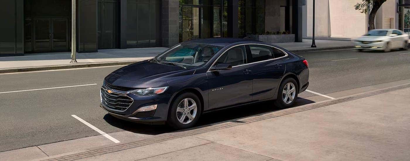 Left angle view of a black 2024 Chevy Malibu parked by a curb.