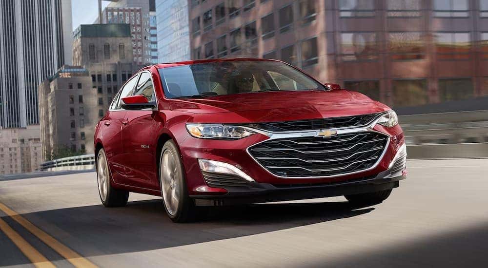 Head-on view of a red 2025 Chevy Malibu driving through a city.