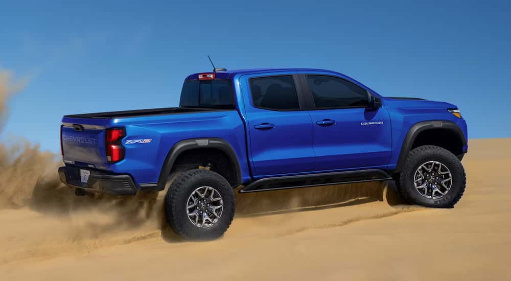 Rear view of a blue 2025 Chevy Colorado ZR2 driving off-road through a desert.